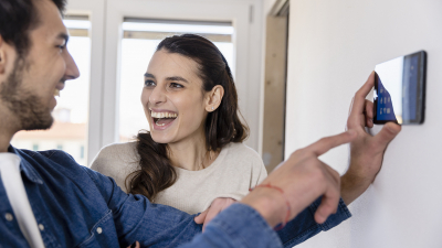 Energiemaßnahmen wollen gut geplant werden. Mann und Frau planen Sanierung im Haus und schauen dabei auf ein Handy und lachen.