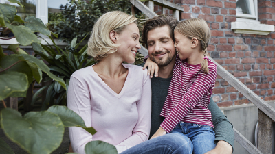 Familie sitzt vor eigenem Haus und genießt zusammen zu sein.