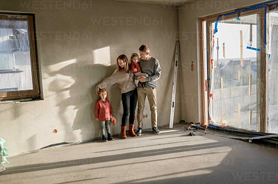 Familie freut sich über den Baufortschritt – Erschließungskosten sind erledigt Glückliche Familie im Rohbau ihres zukünftigen Hauses – Erschließungskosten erfolgreich abgeschlossen.