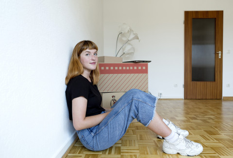 Studentin sitzt in leerer Wohnung an der Wand gelehnt.